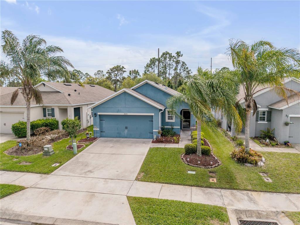 A blue single-story house with a two-car garage and palm trees in the front yard — 2820 TATON TRACE, NEW SMYRNA BEACH, FL
