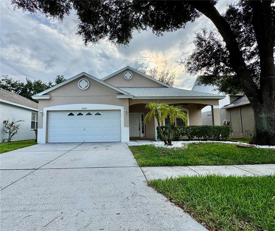 A single-story suburban house with a two-car garage, beige stucco siding, and a front porch — 13052 TERRACE SPRINGS DRIVE, TEMPLE TERRACE, FL