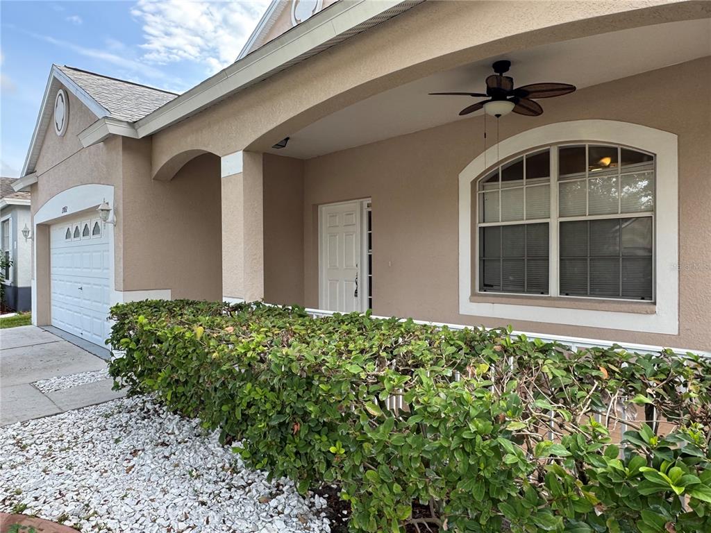 A beige house exterior features a covered porch, a white garage door, and a large hedge — 13052 TERRACE SPRINGS DRIVE, TEMPLE TERRACE, FL