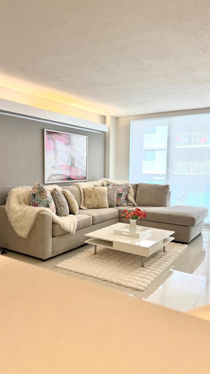 A modern living room features a beige sectional sofa, a white coffee table, and artwork — 6917 Collins Ave # 1206, Miami Beach FL 33141, MIAMI BEACH, FL