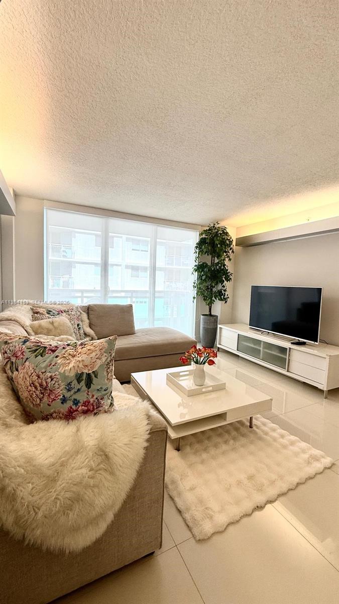 A modern living room features a beige sectional sofa, white coffee table, and television console — 6917 Collins Ave # 1206, Miami Beach FL 33141, MIAMI BEACH, FL