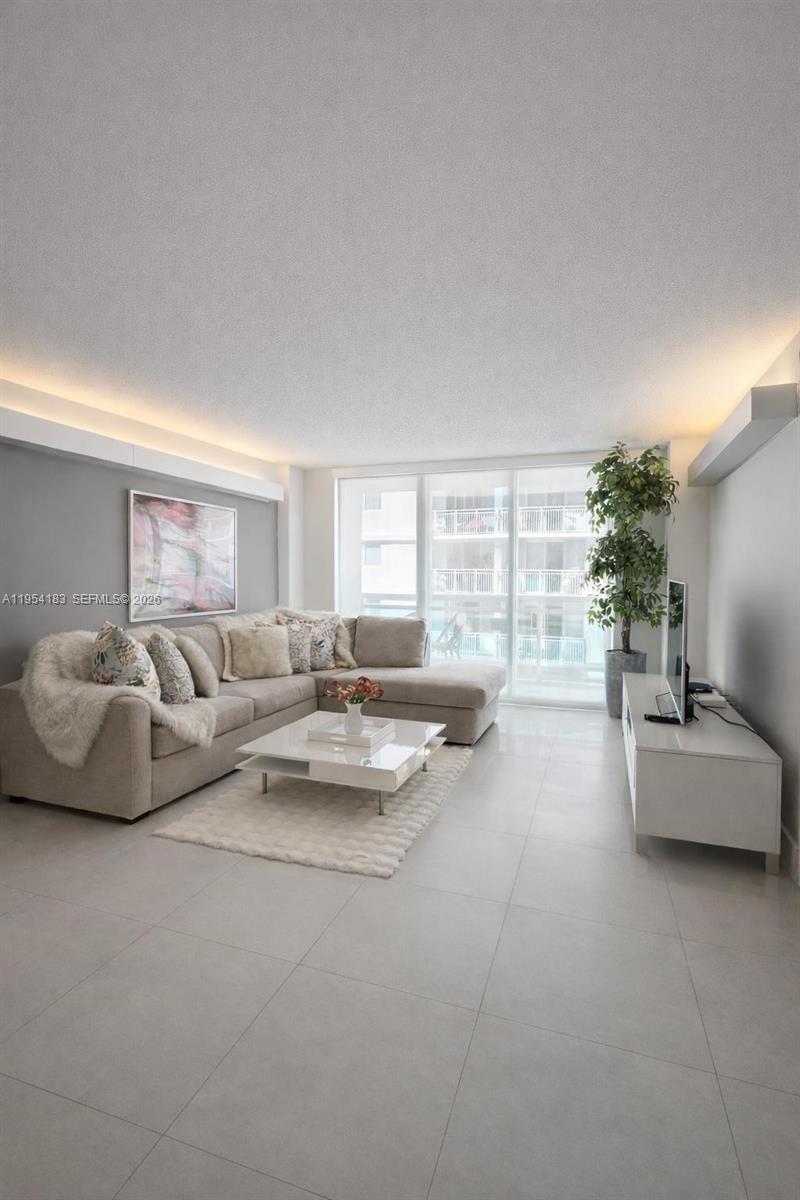 A modern living room features a beige sectional sofa, white coffee table, and tile flooring — 6917 Collins Ave # 1206, Miami Beach FL 33141, MIAMI BEACH, FL