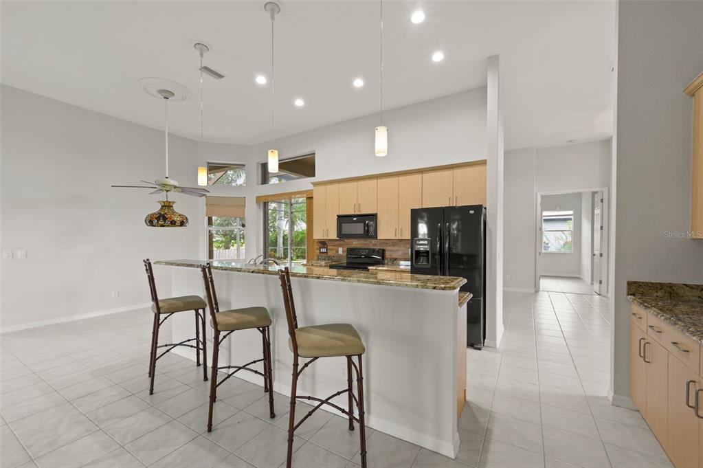 A kitchen with light wood cabinets, granite countertops, and a breakfast bar with three stools — 2727 NW 45TH PLACE, CAPE CORAL, FL