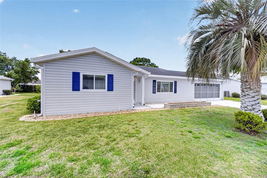A single-story house with light gray siding, blue shutters, and a palm tree in front — 9532 SE 173RD LANE, SUMMERFIELD, FL