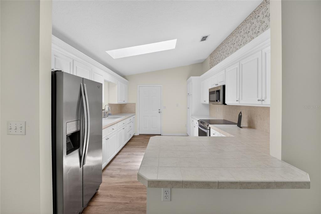 A kitchen features white cabinets, stainless steel appliances, tile countertops, and a skylight — 9532 SE 173RD LANE, SUMMERFIELD, FL