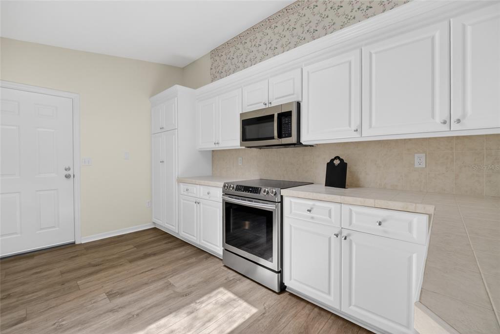A kitchen features white cabinets, stainless steel appliances, tile countertops, and light wood-look flooring — 9532 SE 173RD LANE, SUMMERFIELD, FL