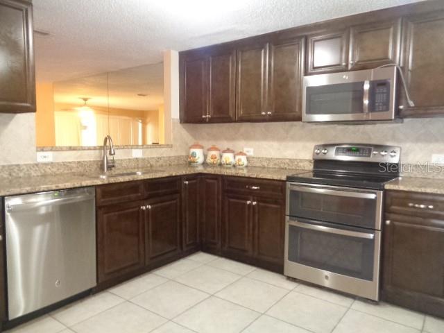 A kitchen features dark wood cabinets, stainless steel appliances, and light-colored tile flooring — 9105 TUDOR DRIVE UNIT 203, TAMPA, FL
