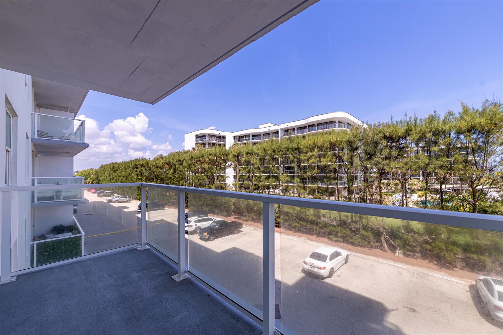 A balcony with a glass railing overlooks a parking lot and a multi-story building — 3450 S Ocean Boulevard # 206, Palm Beach FL 33480, PALM BEACH, FL