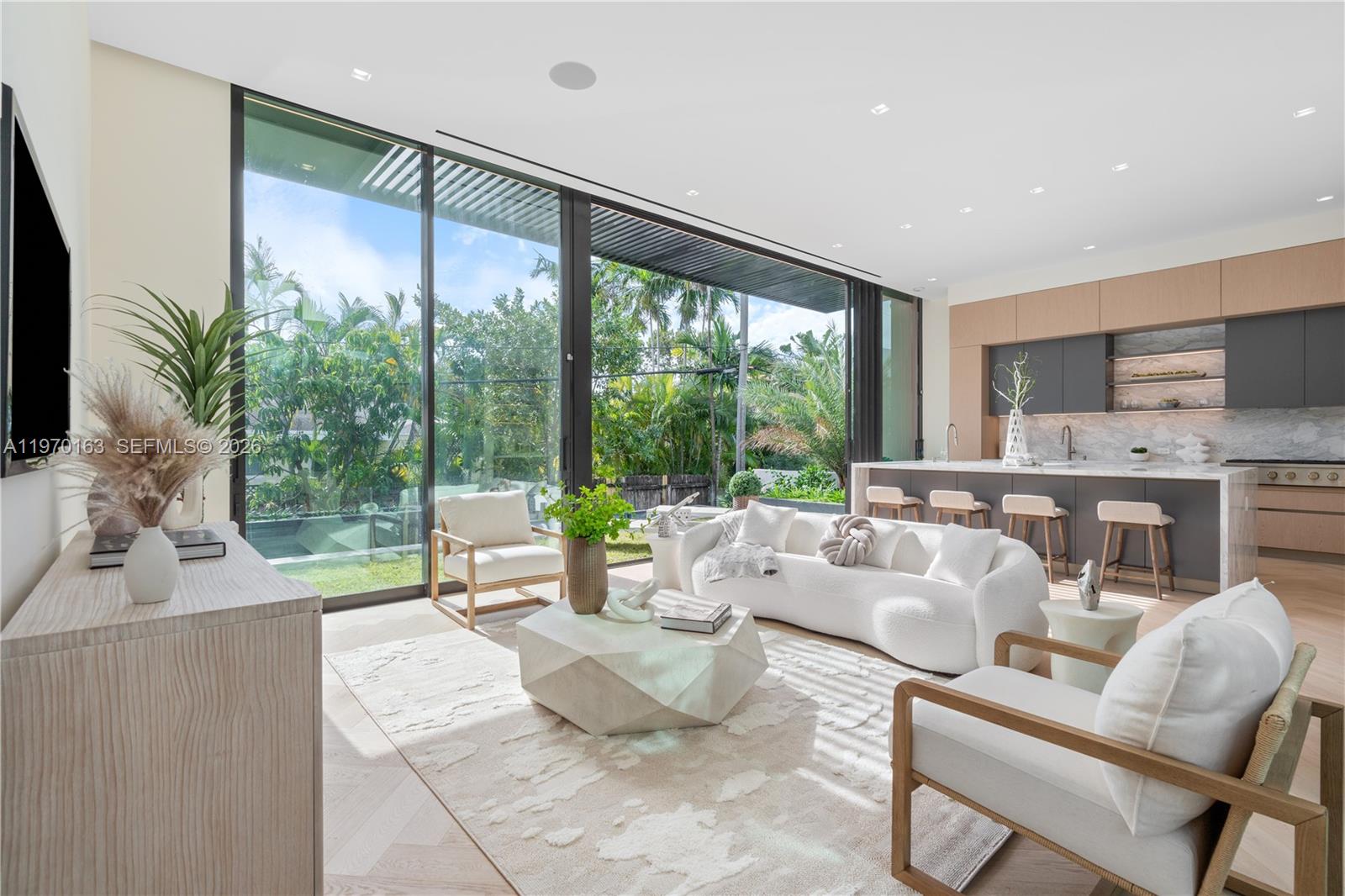 A modern living room and kitchen area features floor-to-ceiling glass doors overlooking a lush garden — 536 W 51st St, Miami Beach FL 33140, MIAMI BEACH, FL