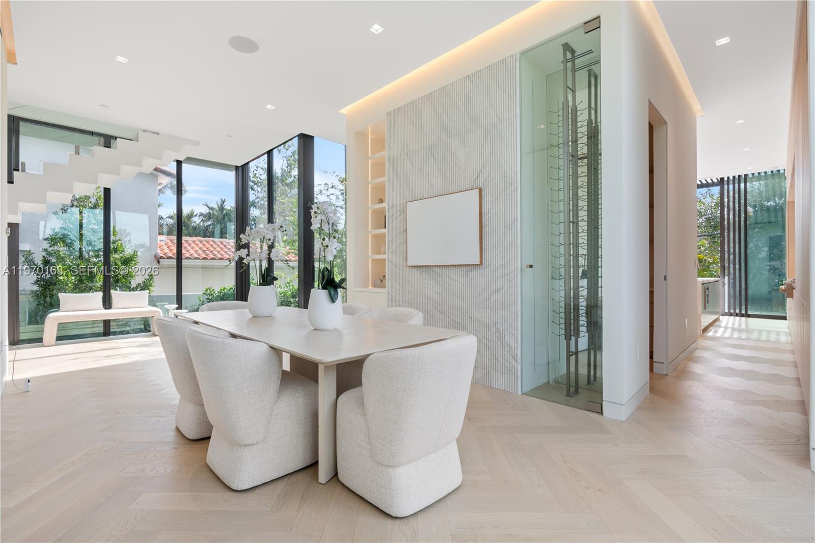 A modern dining room features a glass wine cellar, marble accent wall, and herringbone flooring — 536 W 51st St, Miami Beach FL 33140, MIAMI BEACH, FL