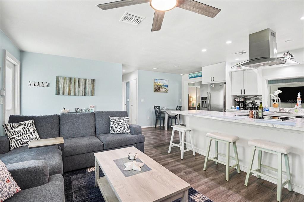 An open-concept living room and kitchen featuring a gray sectional, island seating, and light flooring — 837 DOLPHIN AVENUE NW, PORT CHARLOTTE, FL