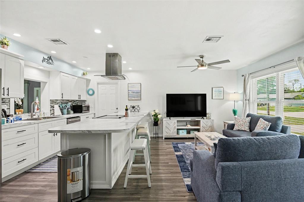 An open-concept kitchen and living area features white cabinetry, a marble island, and blue sofas — 837 DOLPHIN AVENUE NW, PORT CHARLOTTE, FL