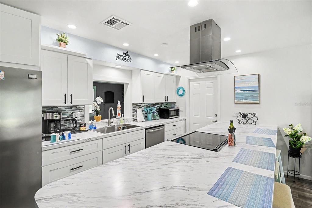 A kitchen features white cabinetry, a large marble-patterned island with a cooktop, and stainless appliances — 837 DOLPHIN AVENUE NW, PORT CHARLOTTE, FL