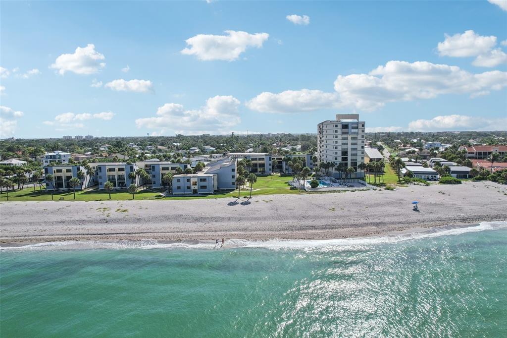 An aerial view shows a multi-story beachfront apartment complex with a pool and sandy beach — 700 GOLDEN BEACH BOULEVARD UNIT 130, VENICE, FL