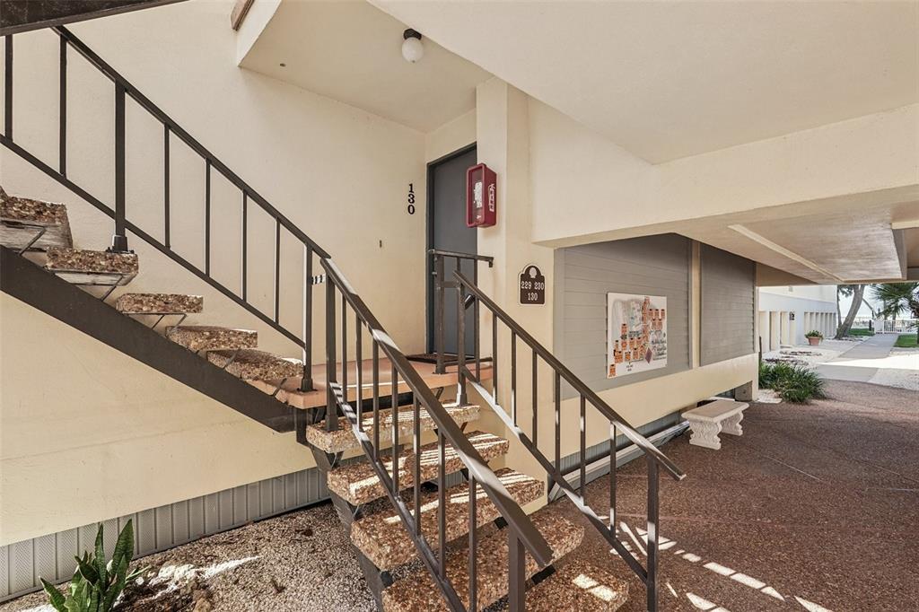 An exterior view of a building entrance with concrete stairs, metal railings, and unit 130 — 700 GOLDEN BEACH BOULEVARD UNIT 130, VENICE, FL