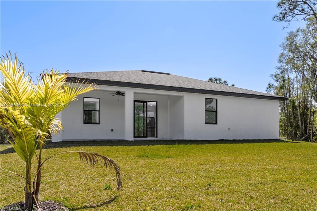 The rear exterior of a white single-story house features a covered patio and lawn — 829 Gillian Ave, Lehigh Acres FL 33974, LEHIGH ACRES, FL