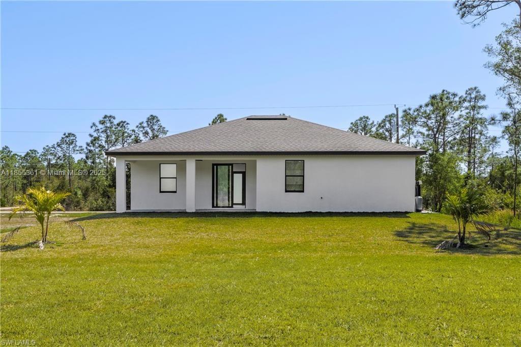 The rear exterior of a white single-story house features a covered patio and lawn — 829 Gillian Ave, Lehigh Acres FL 33974, LEHIGH ACRES, FL