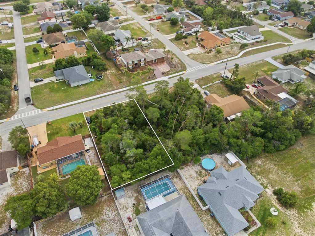 An aerial view shows a vacant, wooded residential lot outlined in white between two houses — 6019 FREEPORT DRIVE, SPRING HILL, FL