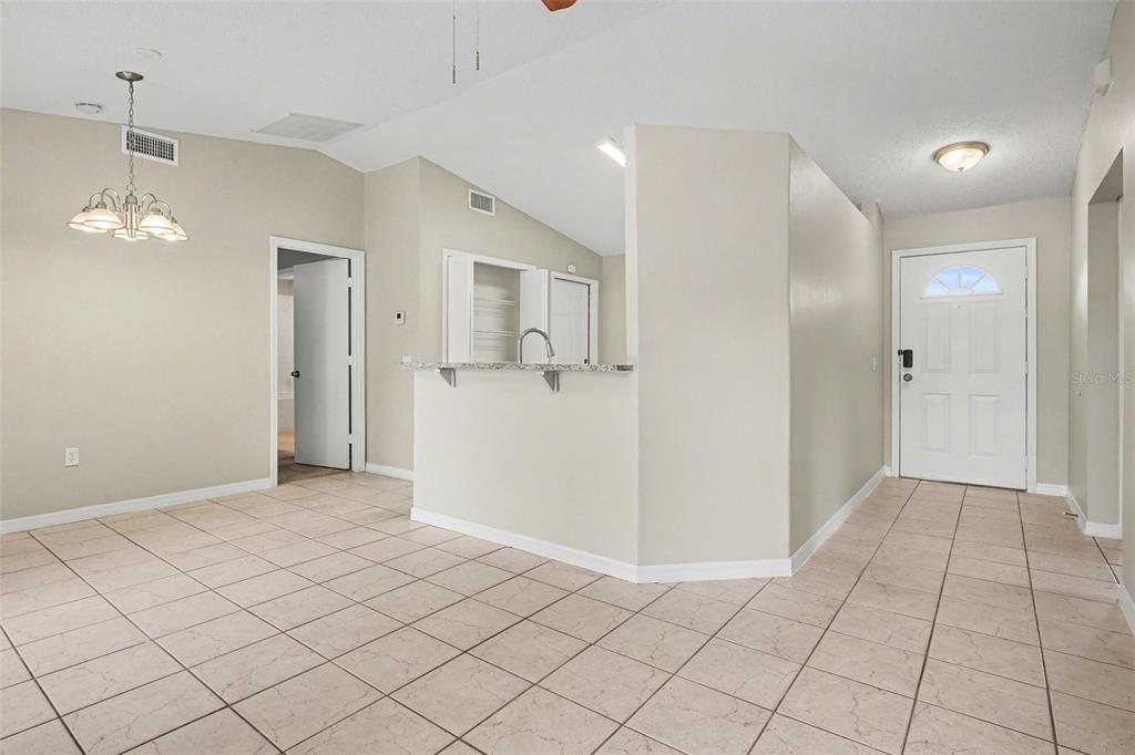An open-concept room features light tile flooring, a kitchen pass-through counter, and an entryway door — 526 N FINCH COURT, KISSIMMEE, FL