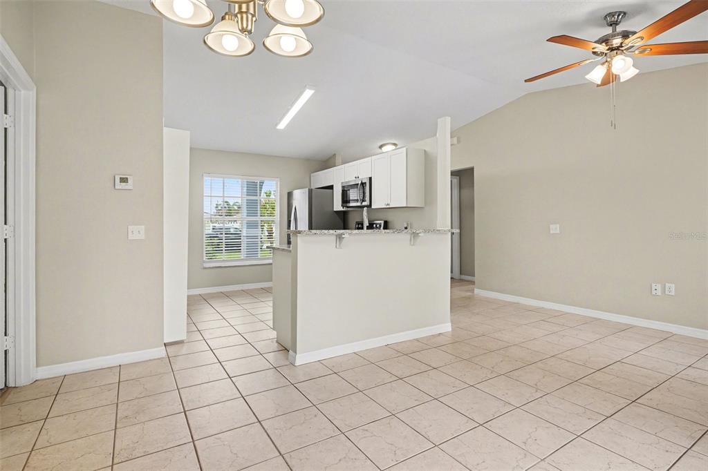A kitchen with white cabinets and granite countertops overlooks a tiled dining and living area — 526 N FINCH COURT, KISSIMMEE, FL