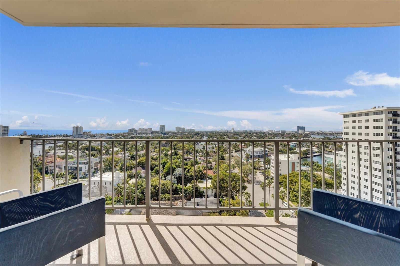 A balcony with two chairs overlooks a city skyline, lush trees, and a distant ocean — 2500 E Las Olas Boulevard # 1509, Fort Lauderdale FL 33301, FORT LAUDERDALE, FL