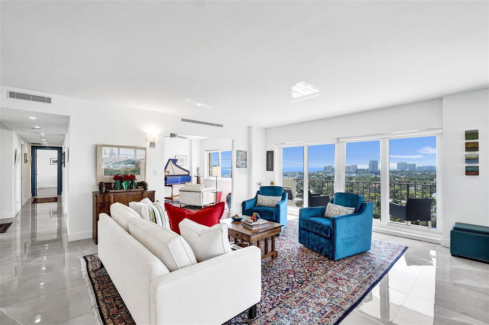 A bright living room features white sofas, blue armchairs, a patterned rug, and floor-to-ceiling windows — 2500 E Las Olas Boulevard # 1509, Fort Lauderdale FL 33301, FORT LAUDERDALE, FL