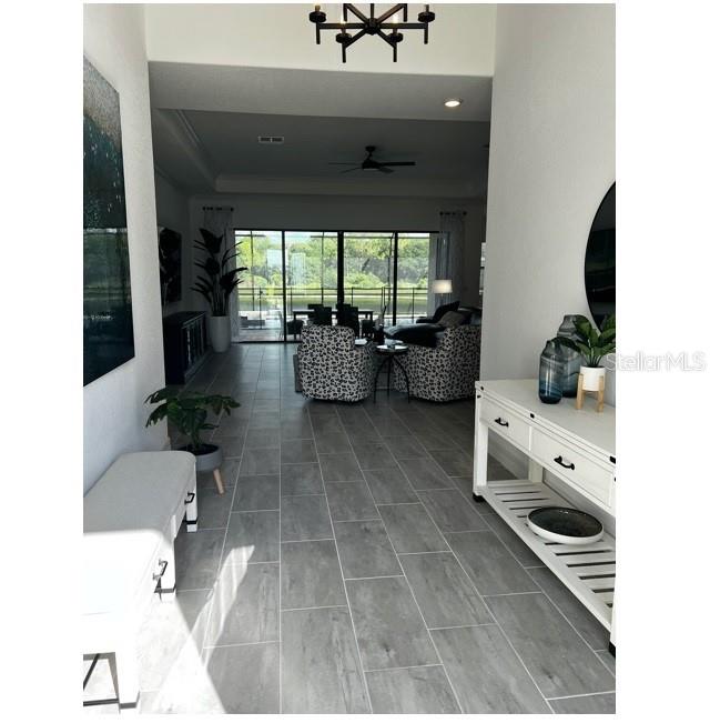 A bright entryway with gray tile flooring leads into a living area with large windows — 17021 POLO TRAIL, LAKEWOOD RANCH, FL