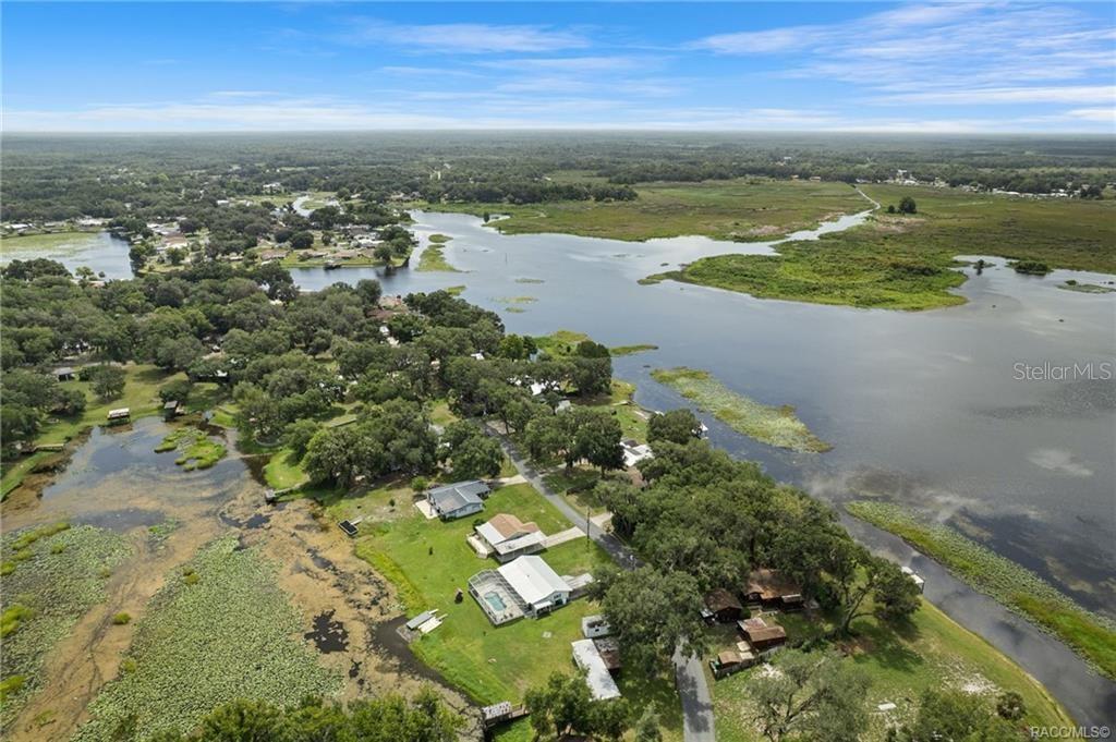 An aerial view shows houses along a lakefront with surrounding trees and marshy water — 8723 E AQUARIUS DRIVE, INVERNESS, FL