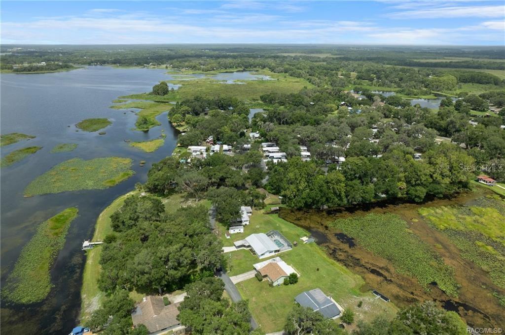 An aerial view shows houses situated along a lakefront with surrounding trees and wetlands — 8723 E AQUARIUS DRIVE, INVERNESS, FL