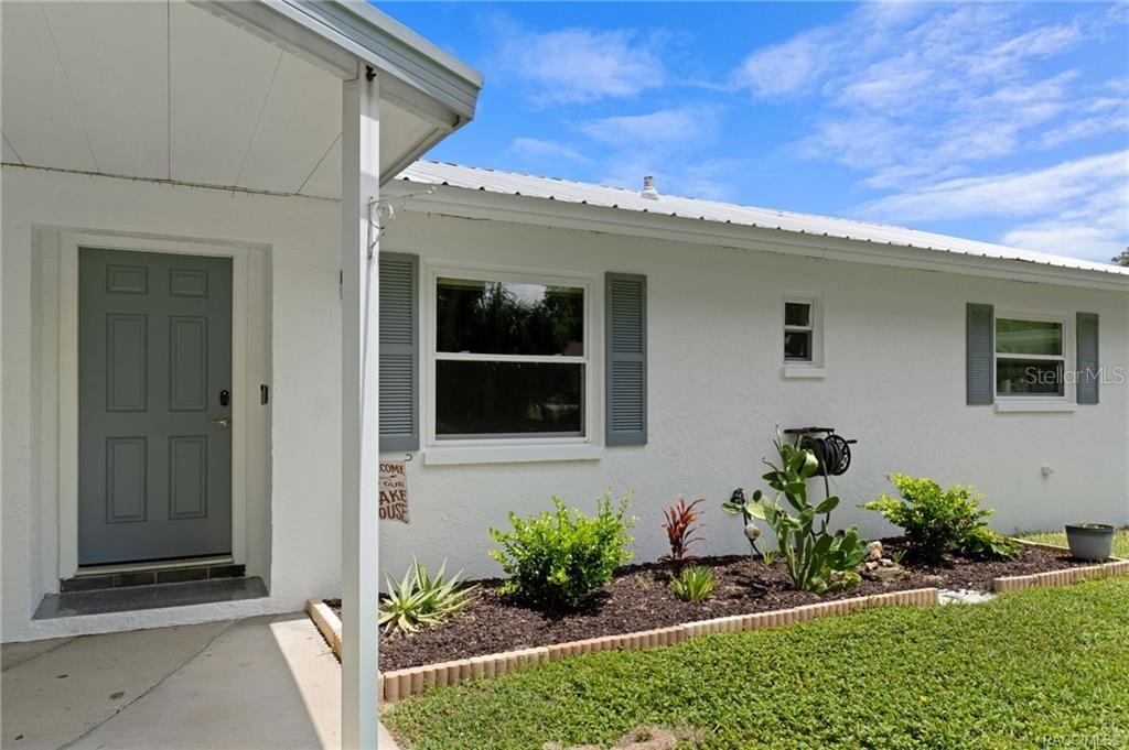 The exterior of a white house features a gray front door and a landscaped garden — 8723 E AQUARIUS DRIVE, INVERNESS, FL