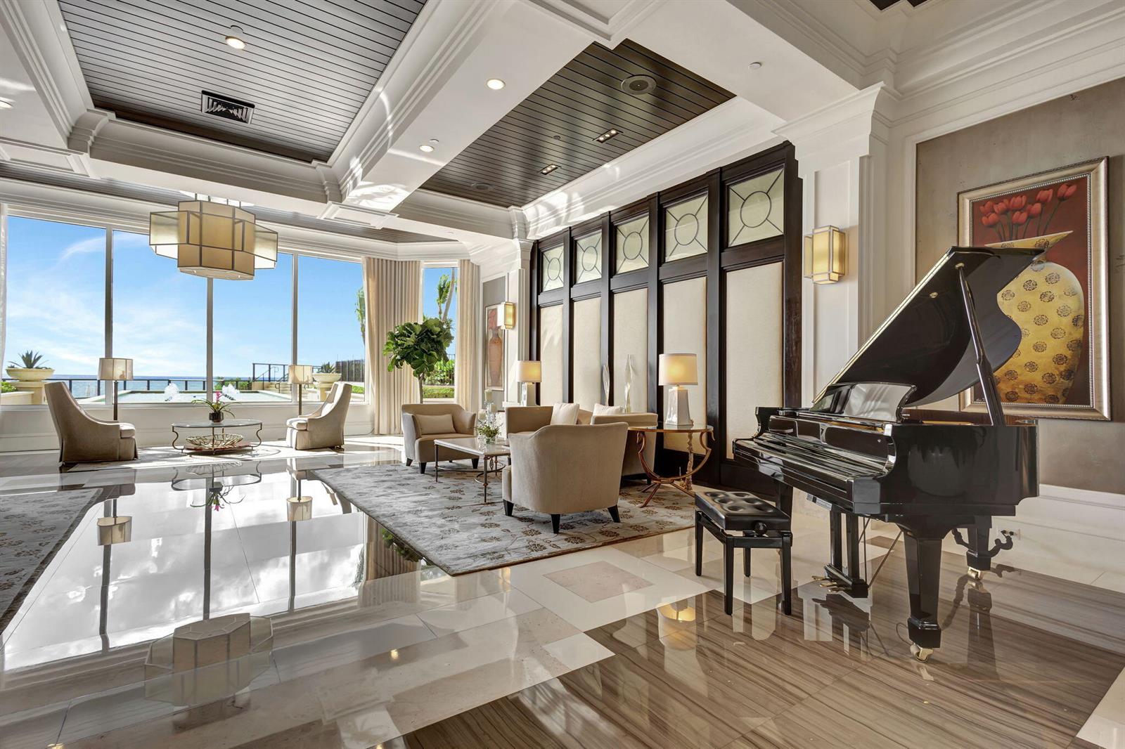 A luxurious living room features a grand piano, marble floors, and floor-to-ceiling windows overlooking water — 2700 N Ocean Drive # 804a, Riviera Beach FL 33404, RIVIERA BEACH, FL