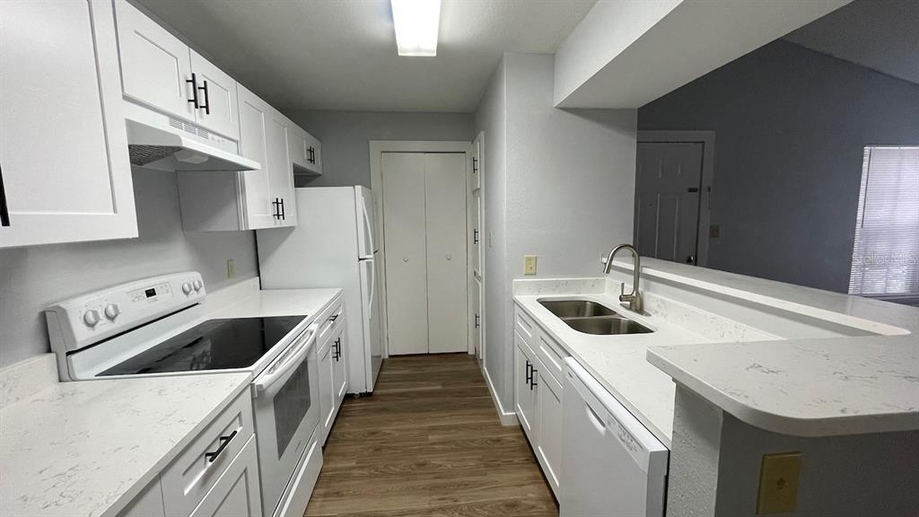 A kitchen features white cabinets, white appliances, quartz countertops, and light wood-look flooring — 4225 THORNBRIAR LANE UNIT 201, ORLANDO, FL