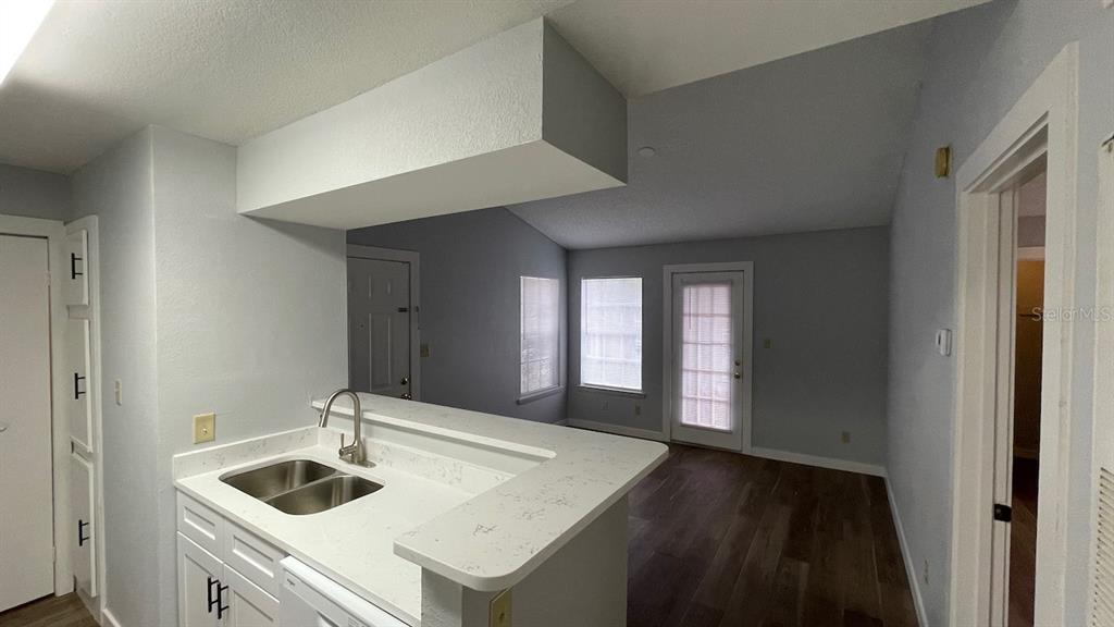 A kitchen with white countertops and cabinets overlooks a living area with wood-look flooring — 4225 THORNBRIAR LANE UNIT 201, ORLANDO, FL