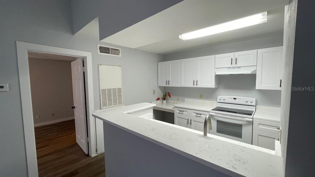 A kitchen features white cabinets, a white stove, and a white countertop breakfast bar — 4225 THORNBRIAR LANE UNIT 201, ORLANDO, FL
