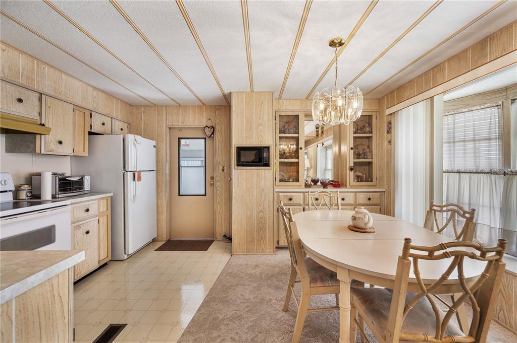A kitchen and dining area featuring wood-paneled walls, cabinetry, a white refrigerator, and carpeted flooring — 1610 REYNOLDS ROAD UNIT 262, LAKELAND, FL