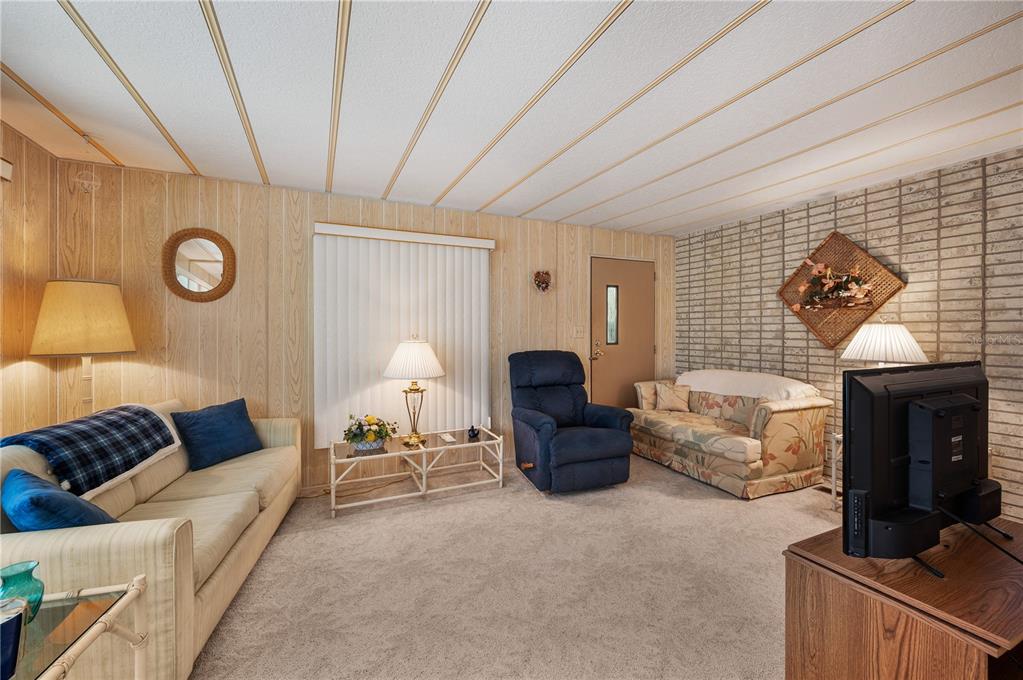 A living room features wood-paneled walls, a brick accent wall, and a drop ceiling — 1610 REYNOLDS ROAD UNIT 262, LAKELAND, FL