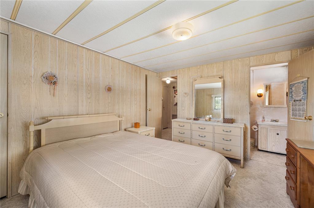 A bedroom with wood-paneled walls, a bed, a dresser with a mirror, and an attached bathroom — 1610 REYNOLDS ROAD UNIT 262, LAKELAND, FL