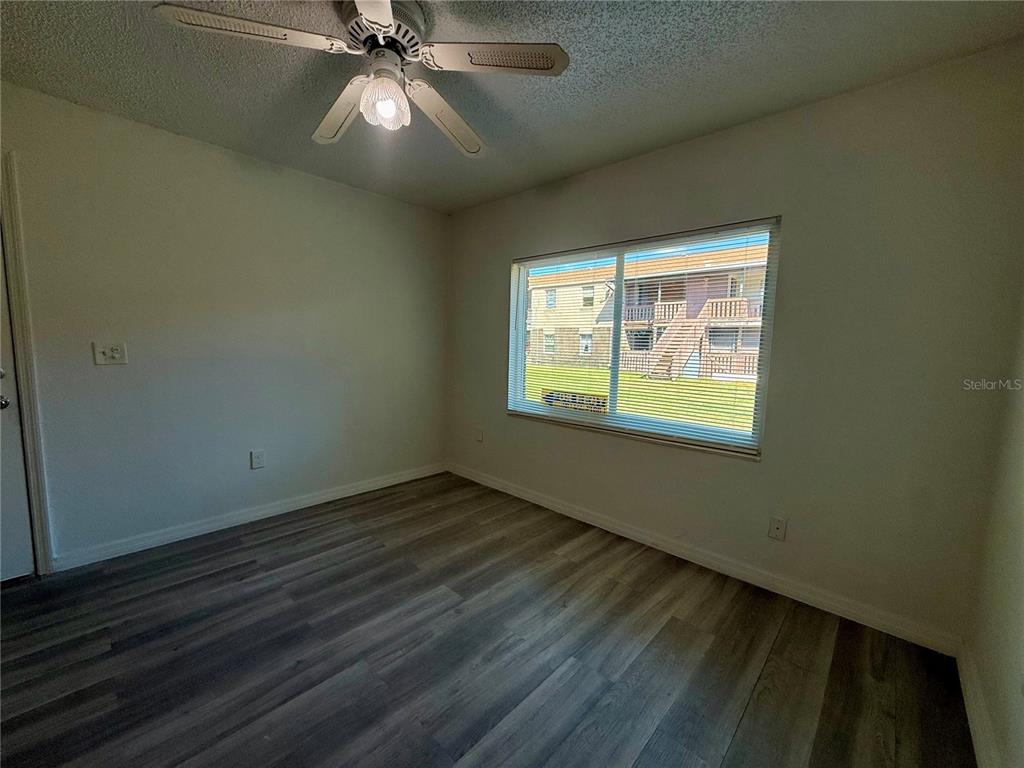 An empty bedroom features gray wood-look flooring, a ceiling fan, and a large window — 9013 WESTCHESTER CIRCLE UNIT 32, TAMPA, FL