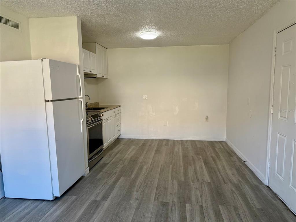 A small kitchen features white cabinets, stainless steel appliances, and gray wood-look flooring — 9013 WESTCHESTER CIRCLE UNIT 32, TAMPA, FL