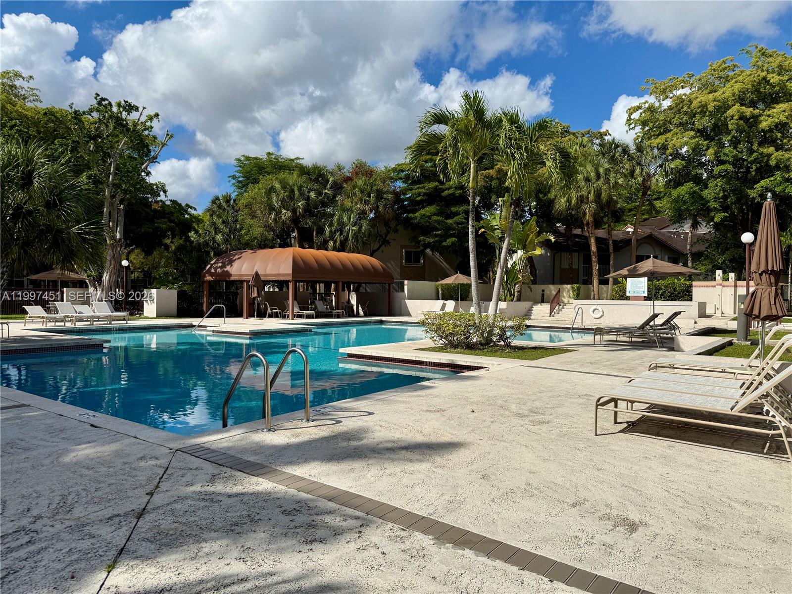An outdoor swimming pool area features lounge chairs, palm trees, and a shaded pavilion — 9435 SW 140th Ct # 9435, Miami FL 33186, MIAMI, FL