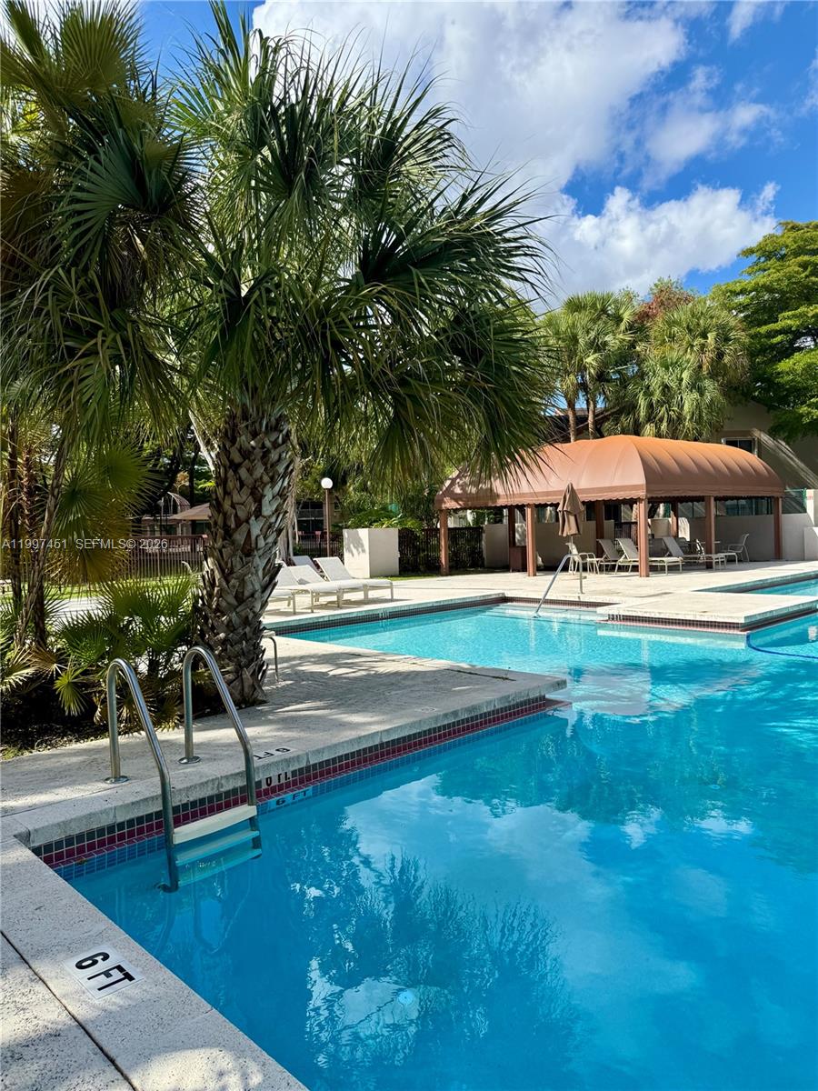 A swimming pool with a metal ladder and a palm tree sits beside a shaded patio — 9435 SW 140th Ct # 9435, Miami FL 33186, MIAMI, FL