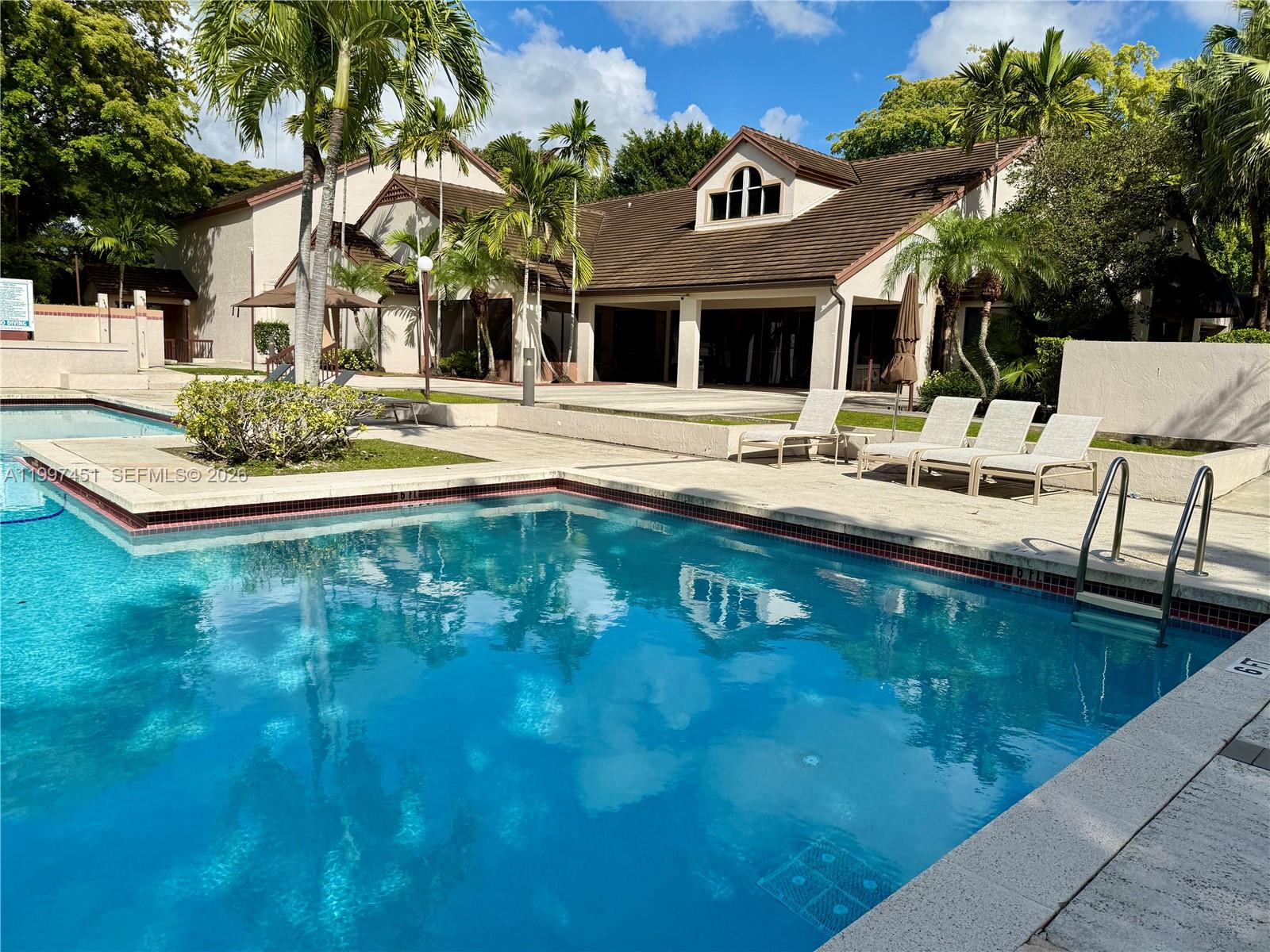 A swimming pool with lounge chairs sits in front of a multi-story building with palms — 9435 SW 140th Ct # 9435, Miami FL 33186, MIAMI, FL