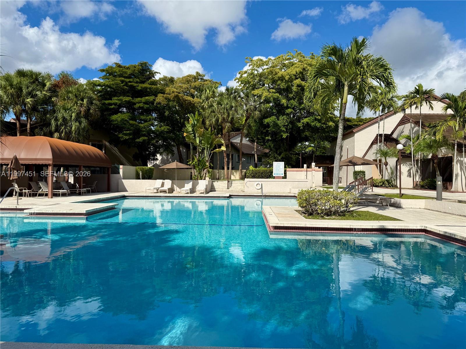 A swimming pool with a brown canopy and lounge chairs surrounded by trees and buildings — 9435 SW 140th Ct # 9435, Miami FL 33186, MIAMI, FL