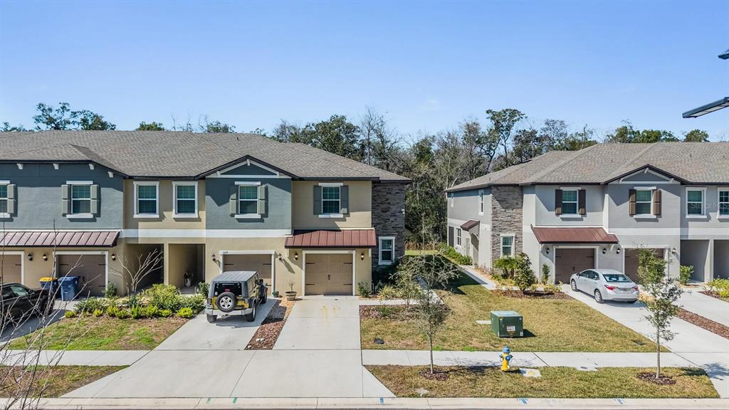 An exterior view of two-story townhomes with garages, driveways, and a grassy lawn — 11123 WISHING CLOUD ROAD, LAND O LAKES, FL