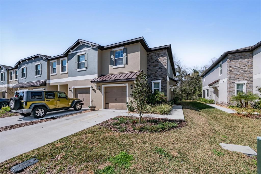 A two-story townhouse with a stone facade, a garage, and a parked yellow Jeep — 11123 WISHING CLOUD ROAD, LAND O LAKES, FL