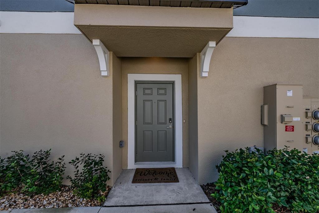 A gray front door with a welcome mat sits under a small covered entryway — 11123 WISHING CLOUD ROAD, LAND O LAKES, FL