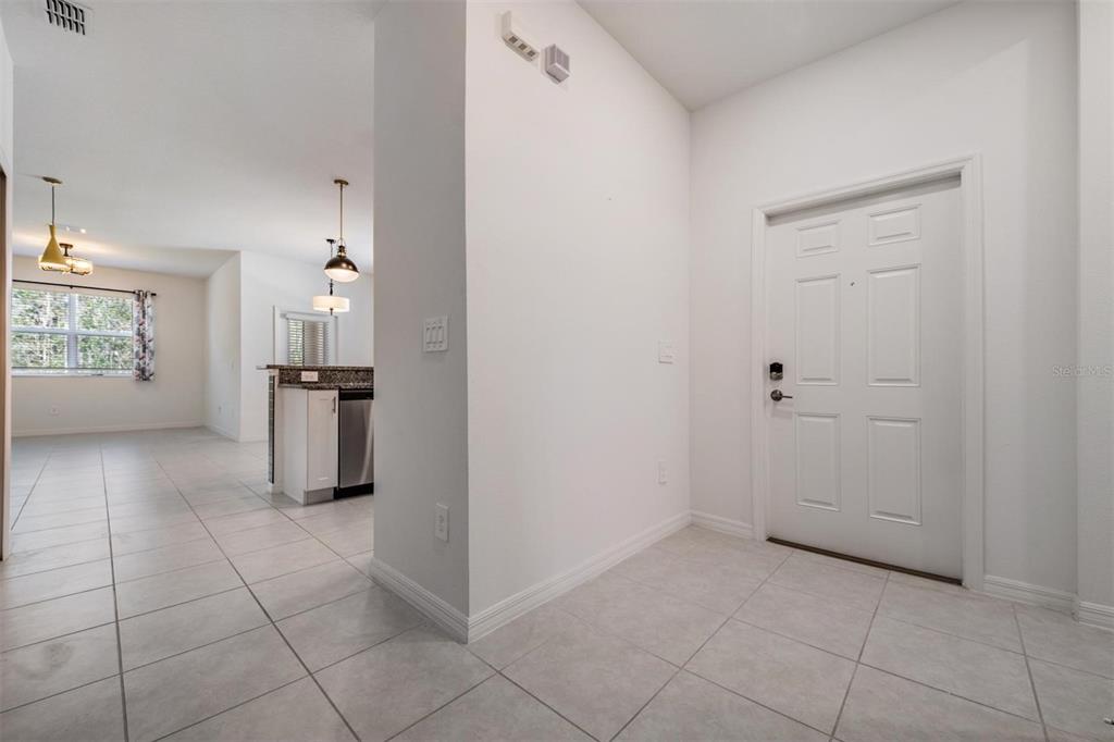 A white front door opens into a tiled entryway next to an open-concept kitchen — 11123 WISHING CLOUD ROAD, LAND O LAKES, FL