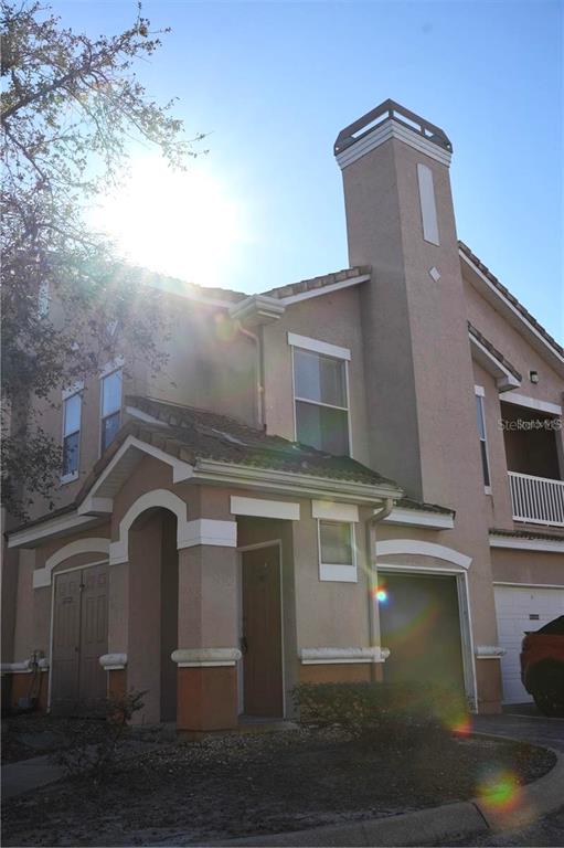 A two-story tan stucco townhouse features a chimney, a covered entryway, and an attached garage — 10446 VILLA VIEW CIRCLE, TAMPA, FL