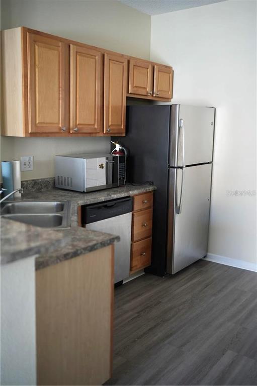 A kitchen features light wood cabinets, stainless steel appliances, and dark gray laminate flooring — 10446 VILLA VIEW CIRCLE, TAMPA, FL