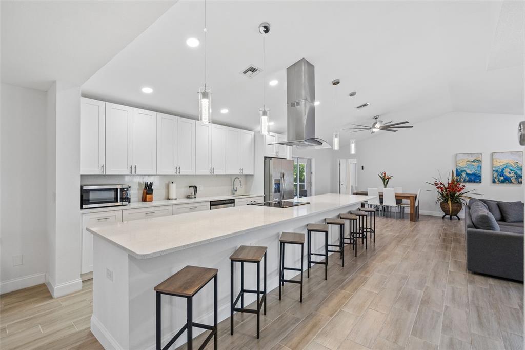 A modern kitchen features white cabinetry, a long quartz island with bar stools, and flooring — 1192 ALTON RD, PORT CHARLOTTE, FL